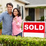 Hispanic couple outside home with sold sign. Relocating and need to sell house fast