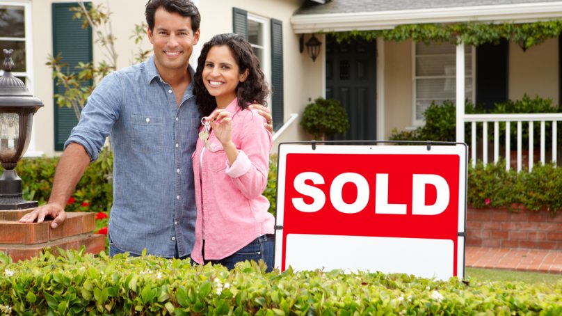 Hispanic couple outside home with sold sign. Relocating and need to sell house fast